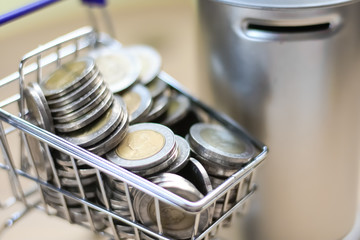 Many coins are in the mini shopping cart with coin bank. Saving money concept.