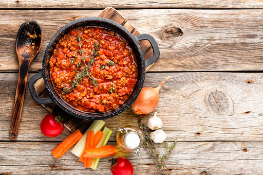 classic italian bolognese sauce stewed in cauldron with ingredients on wooden table, top view, culinary background with space for text