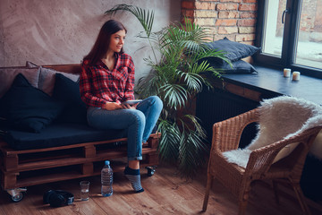 Obraz premium Charming brunette in a flannel shirt and jeans sitting on a couc