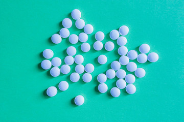 A pile of little white pills on green background