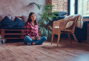 Fototapeta na wymiar Charming brunette in a flannel shirt and jeans sitting on a floo