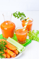 Carrot juice in beautiful glasses, cut orange vegetables and green parsley on white wooden background. Fresh orange drink. Close up photography. Selective focus. Vertical banner