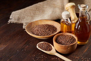 Flax seeds in bowl and flaxseed oil in glass bottle on wooden background, top view, close-up, selective focus
