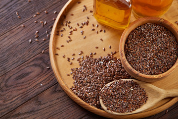 Flax seeds in bowl and flaxseed oil in glass bottle on wooden background, top view, close-up, selective focus