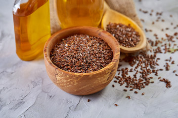 Flax seeds in bowl and flaxseed oil in glass bottle on light textured background, top view, close-up, selective focus