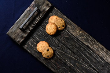 Chip-cookies on a dark old wooden trayon a blue background.