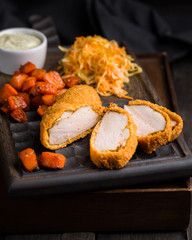 Gourmet delicious crispy fried chicken breast (nuggets) with a spicy sauce and served with chopped fresh herbs, caramelized carrots and cabbage salad on an old rustic wooden chopping board