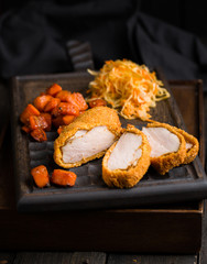 Gourmet delicious crispy fried chicken breast (nuggets) with a spicy sauce and served with chopped fresh herbs, caramelized carrots and cabbage salad on an old rustic wooden chopping board