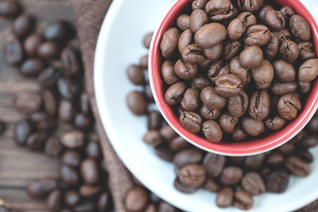 Roasted coffee bean in red cup on wodden table surrounded by coffee bean