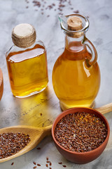 Flax seeds in bowl and flaxseed oil in glass bottle on light textured background, top view, close-up, selective focus