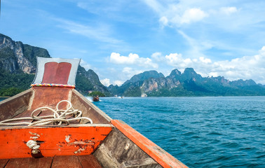 Wooden Thai traditional long-tail boat on a lake with mountains and rain forest in the background during a sunny day at Ratchaprapha Dam at Khao Sok National Park, Surat Thani Province, Thailand