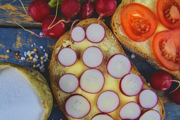 Spread butter on bread with sliced tomatoes and radishes. Fresh snack on natural wooden background. Flat design. Top view