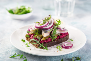 open sanwich with dark rye bread, beet, marinated herring, pickled cucumber and red onion, smorrebrod