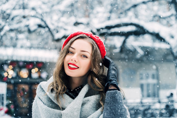 Outdoor close up portrait of young beautiful happy smiling girl with red lips, wearing beret, posing in street of european city. Winter fashion, holidays concept
