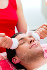 Obraz na płótnie Canvas Man having relaxing herbal bag face massage in wellness spa 