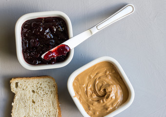 Peanut butter and jelly in bowls with knife and slice of bread on grey background - Top view image