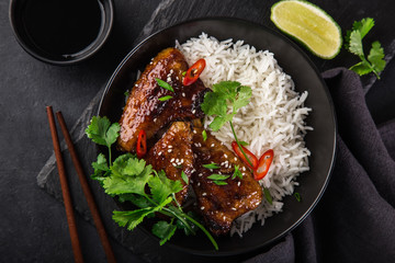 bowl of teriyaki chicken wings and rice served with lime, cilantro and sesame seeds