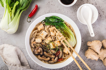 asian vegan noodle soup with tofu cheese,shiitake mushroms and pak choi in white bowl and...
