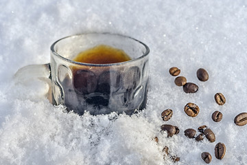 A mug of black coffee stands in the snow, scattered beans