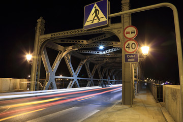 Zabytkowy most nitowany w Brzegu nad rzeką Odrą w nocy, światła camochodów.