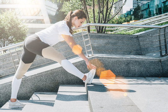 Sunny summer day. Young woman in sportswear doing stretching exercises outdoor. Girl doing warm-up on steps before training. Exercise in street, sports exercises, workout.
