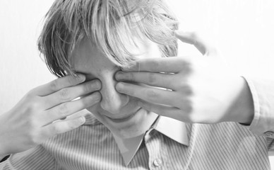 Teen boy closes his eyes with his hands
