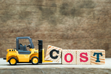 Yellow toy forklift hold letter block C to complete word cost on wood background