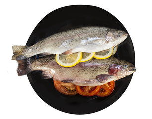 Two fresh trout on a black plate with tomatoes and lemon. The view from the top.