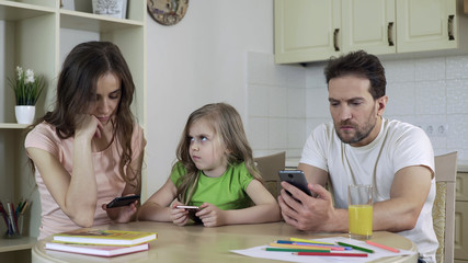 Man and woman focused on smartphones, little daughter needs parents attention