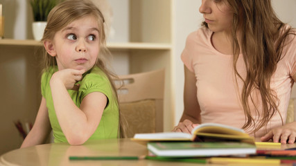 Bored daughter surprisedly looking to mother making her to do homework