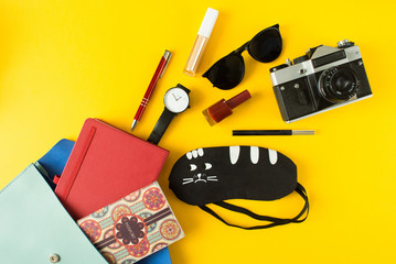 Flat lay of cute woman bag open out with passport, old camera, sunglasses, notebook, accessories and nail polish on colorful background with copy space, top view. All you need to comfort travel.