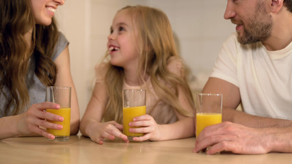 Happy healthy family drinking orange juice with smiles on faces, morning at home