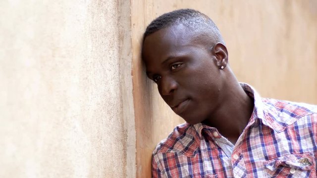 sad and depressed  young african black man leaning against the wall- outdoor