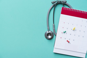 Top view of stethoscope and calendar on the green background, schedule to check up healthy concept