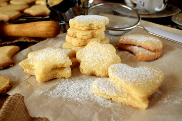 Shaped shortbread cookies covered with sugar powder surrounded by kitchen utensils