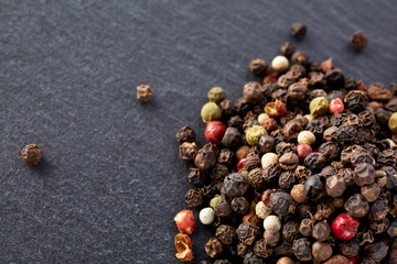 Top view on composition of peppercorns in wooden spoon on dark background, close-up.