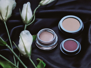 Single neutral eyeshadows on black satin fabric next to white flowers. 