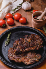 Fried steak with seasonings in an iron plate on a wooden table. tomatoes pepper garlic.