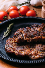 Fried steak with seasonings in an iron plate on a wooden table. tomatoes pepper garlic.