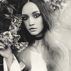 Beautiful young woman surrounded by flowers of lilac