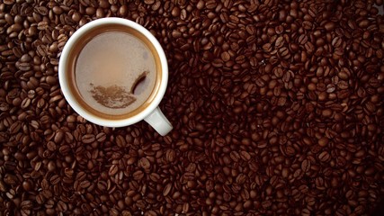top view of cup of black coffe put it on coffe beans background. White cup of black coffee