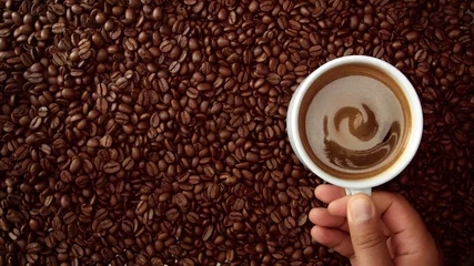 Crédence de cuisine en verre imprimé Café vue de dessus de la main avec une tasse de café noir le mettre sur fond de grains de café. Tasse blanche de café noir