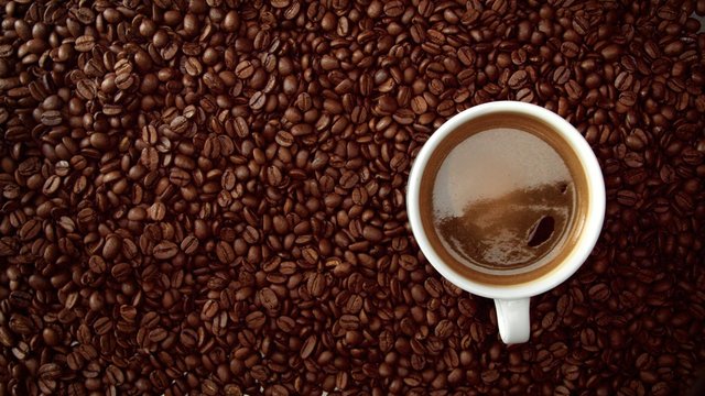 top view of cup of black coffe put it on coffe beans background. White cup of black coffee