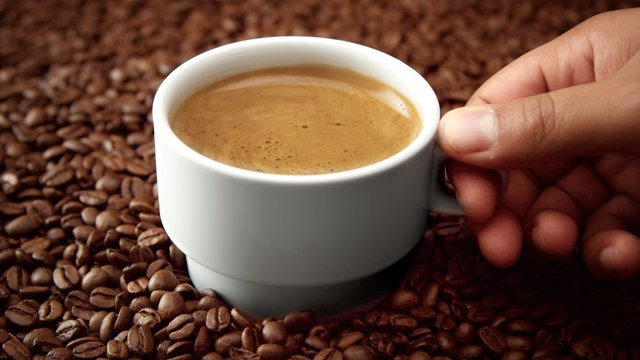 side view of white cup of black coffe on coffee beans. Coffee cream moving in cup