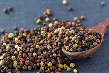 Top view on composition of peppercorns in wooden spoon on dark background, close-up.