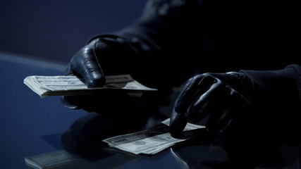 Criminal in black gloves counting bundle of money earned for committing crime