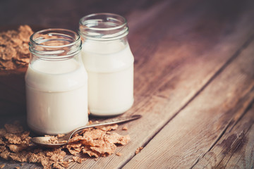 Two milk bottles and cereal wheat flakes in bowl for breakfast on wooden table. Copy space for text.