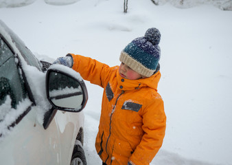European boy cleans the car from snow