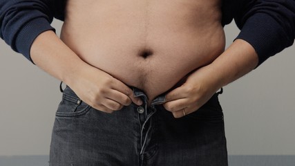 Naklejka premium overweight man closeup of belly side view. put up shirt and pinch and clap a belly
