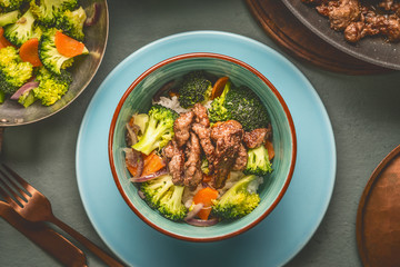 Close up of healthy balanced nutrition meal in bowl with beef meat, rice , steamed vegetables: broccoli and carrots served with plate and cutlery, top view